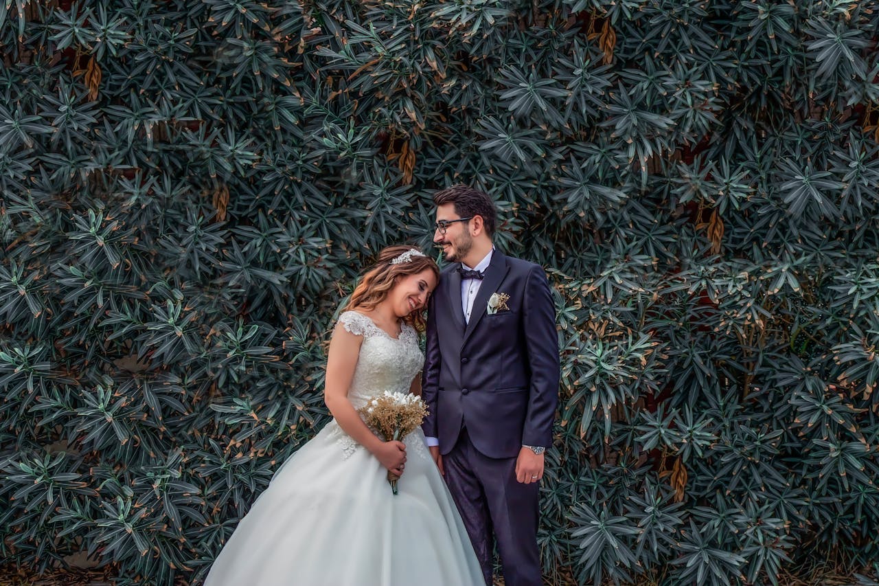 Woman in White Wedding Dress Holding Bouquet of Flowers Leaning on Man in Black Suit